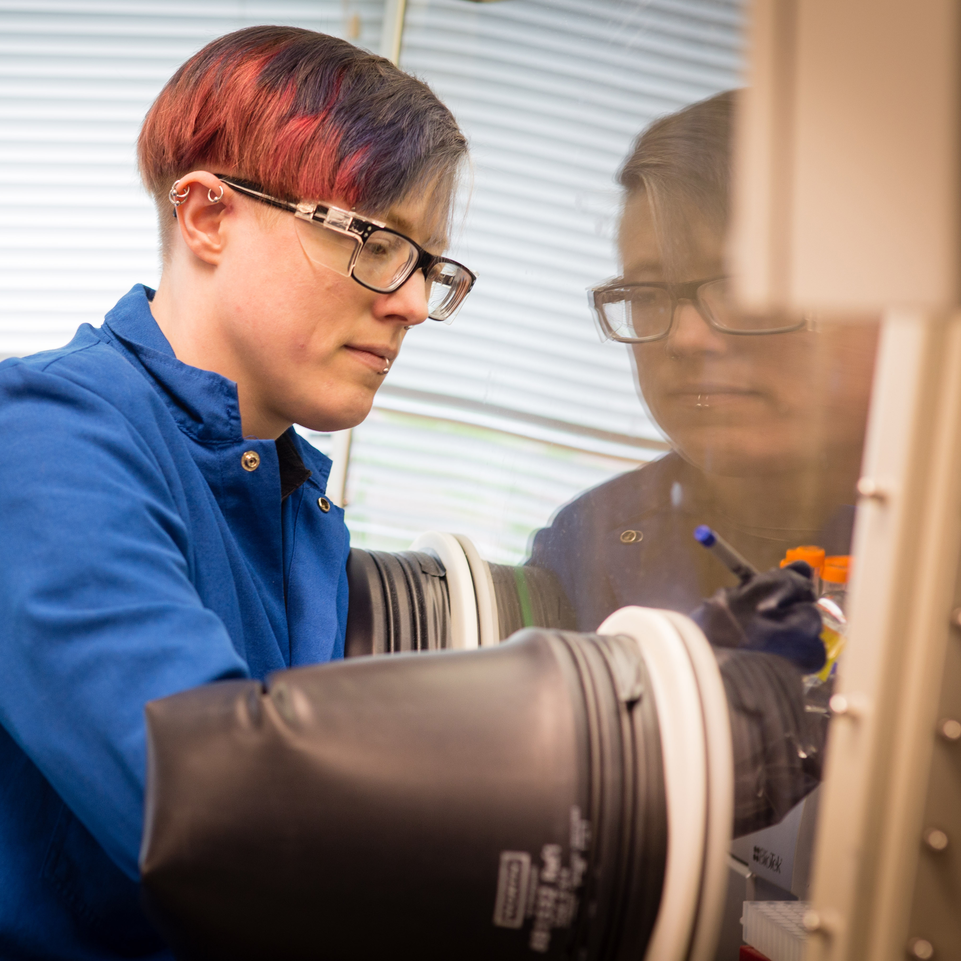 a photo of dr. g. e. kenney in a blue lab coat working in a glovebox